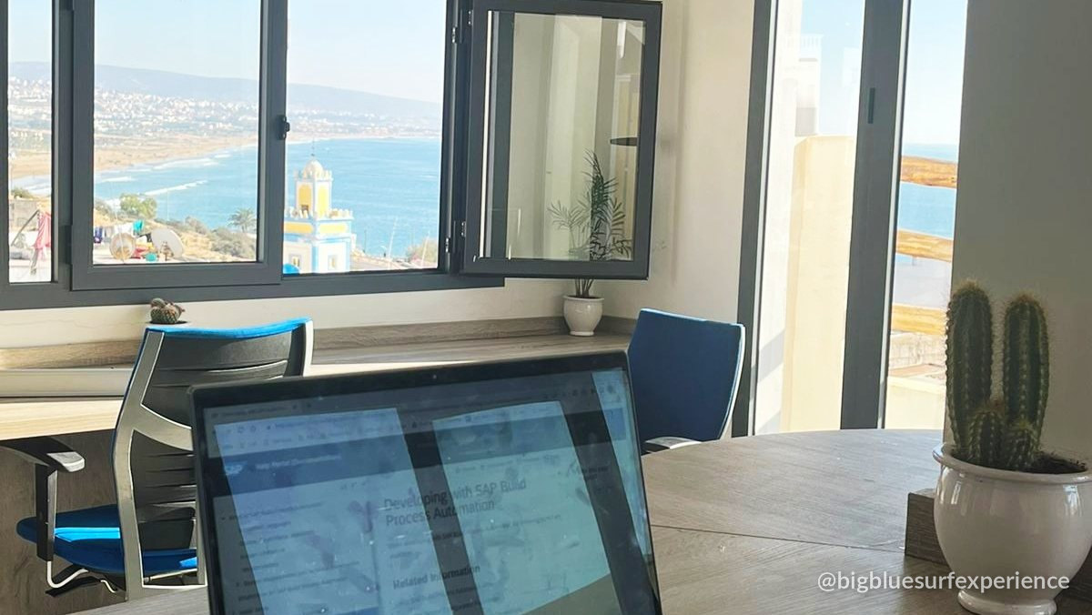 Laptop on a wooden desk facing the bay through open windows at the BigBlue coworking space