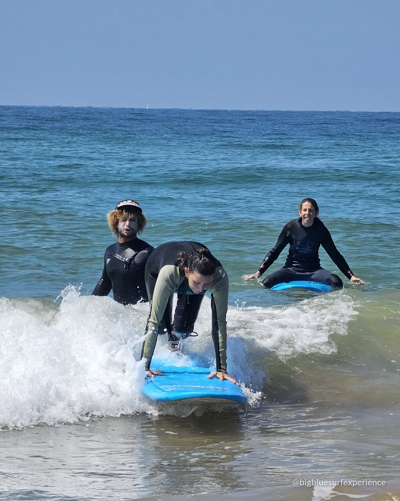BigBlue guest popping up on a blue surfboard in the whitewater, coach watching behind
